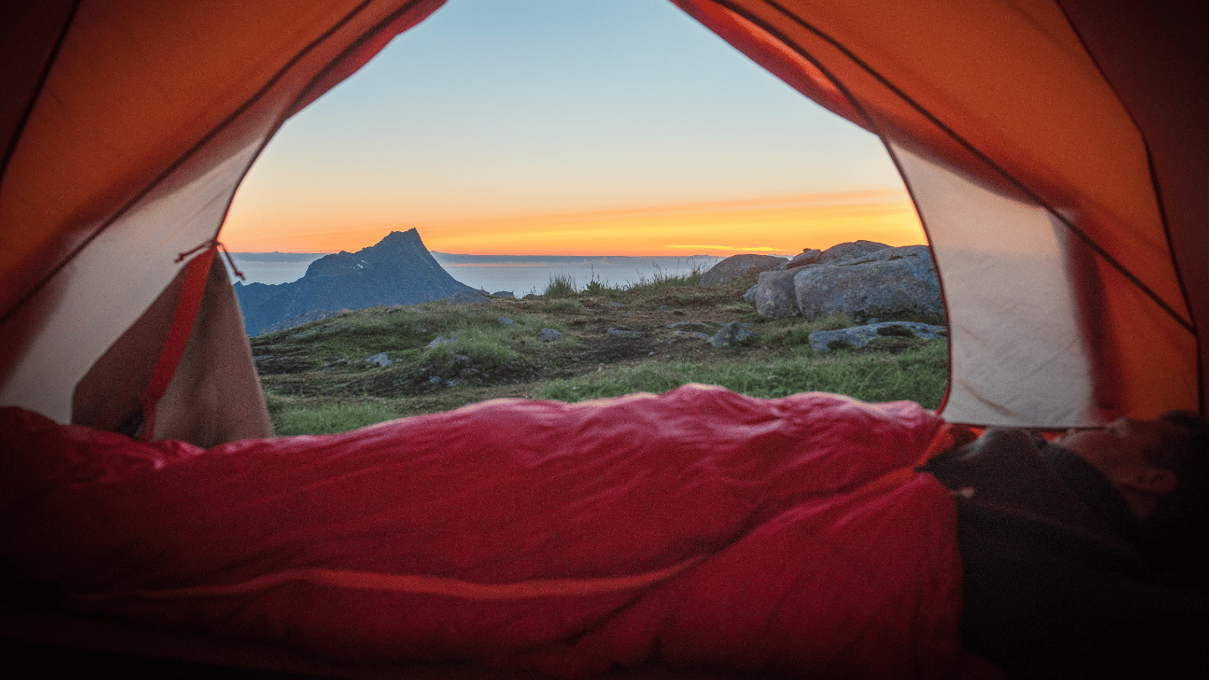 photo dans une tente de bivouac une femme assise dans son duvet à côté d'une tente.